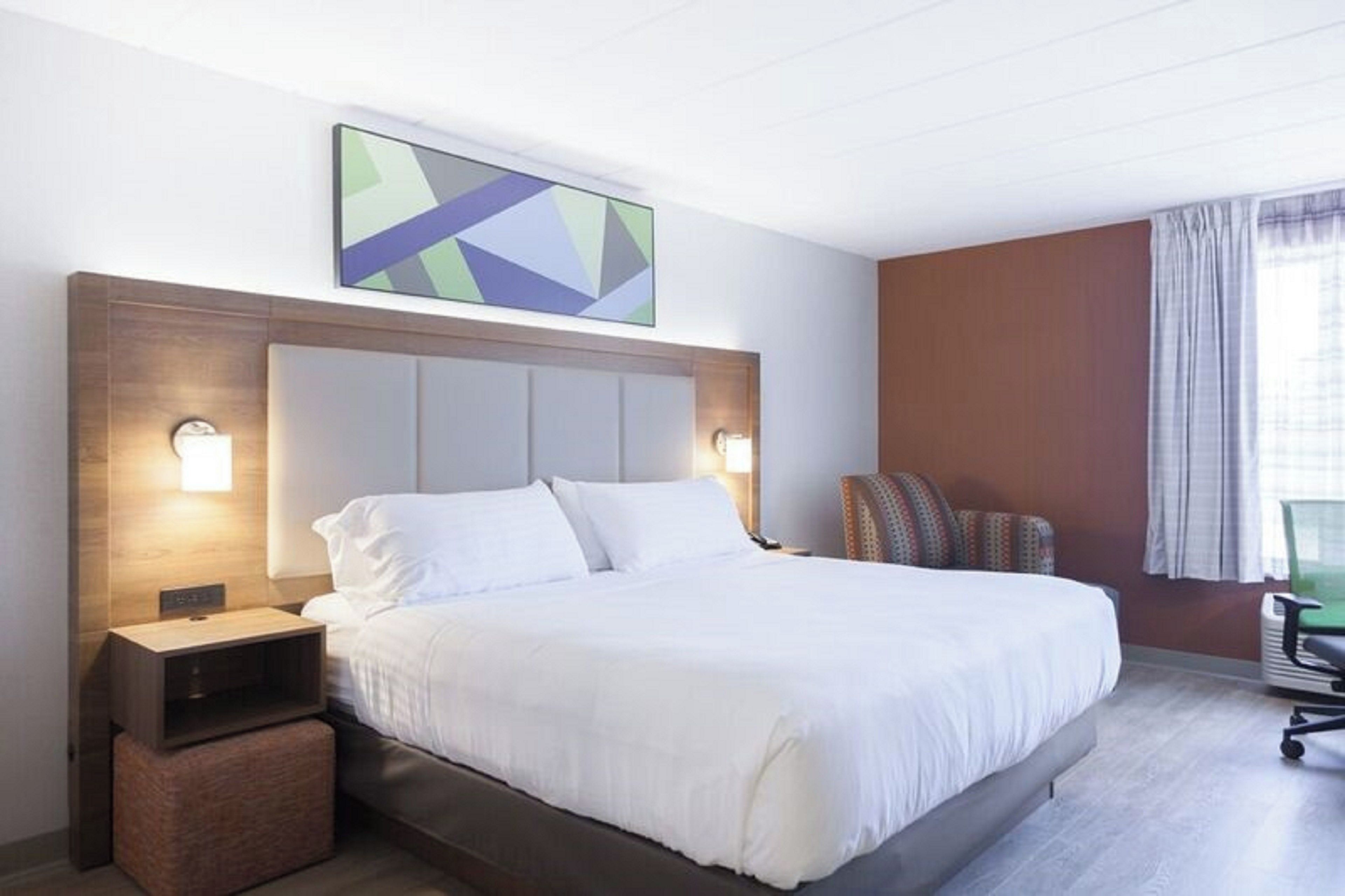 A hotel room with a large bed, a nightstand, a chair, and a painting on the wall.