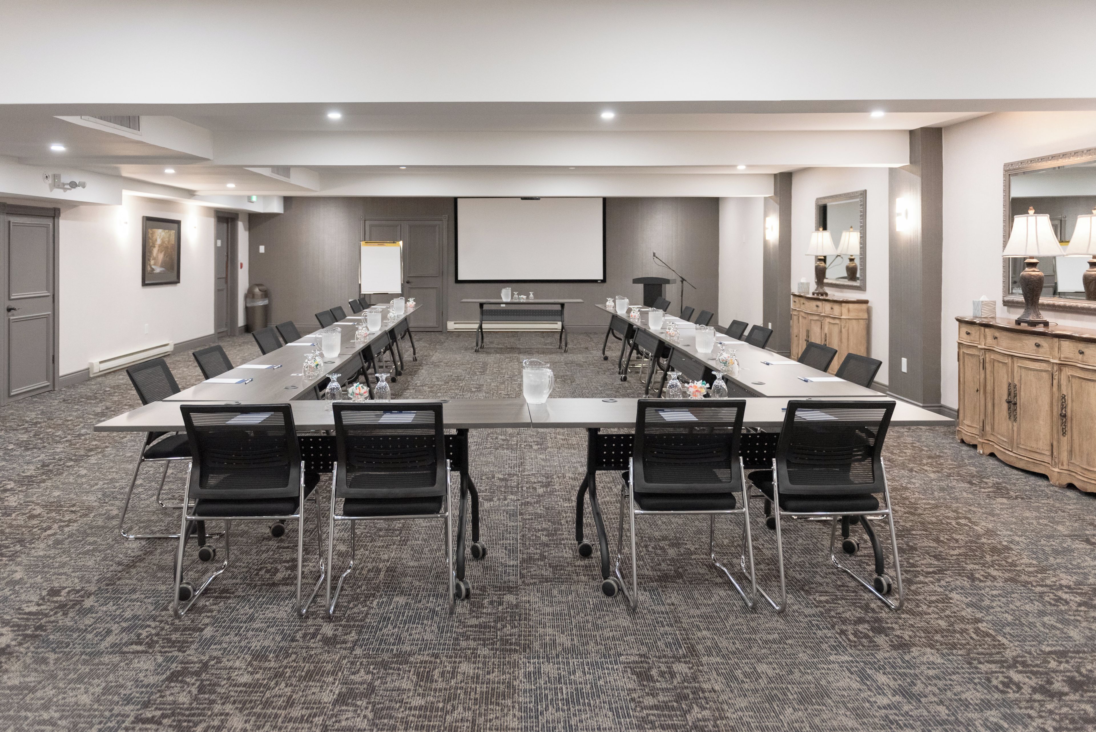 A conference room with a long table, chairs, a projector screen, and a podium.
