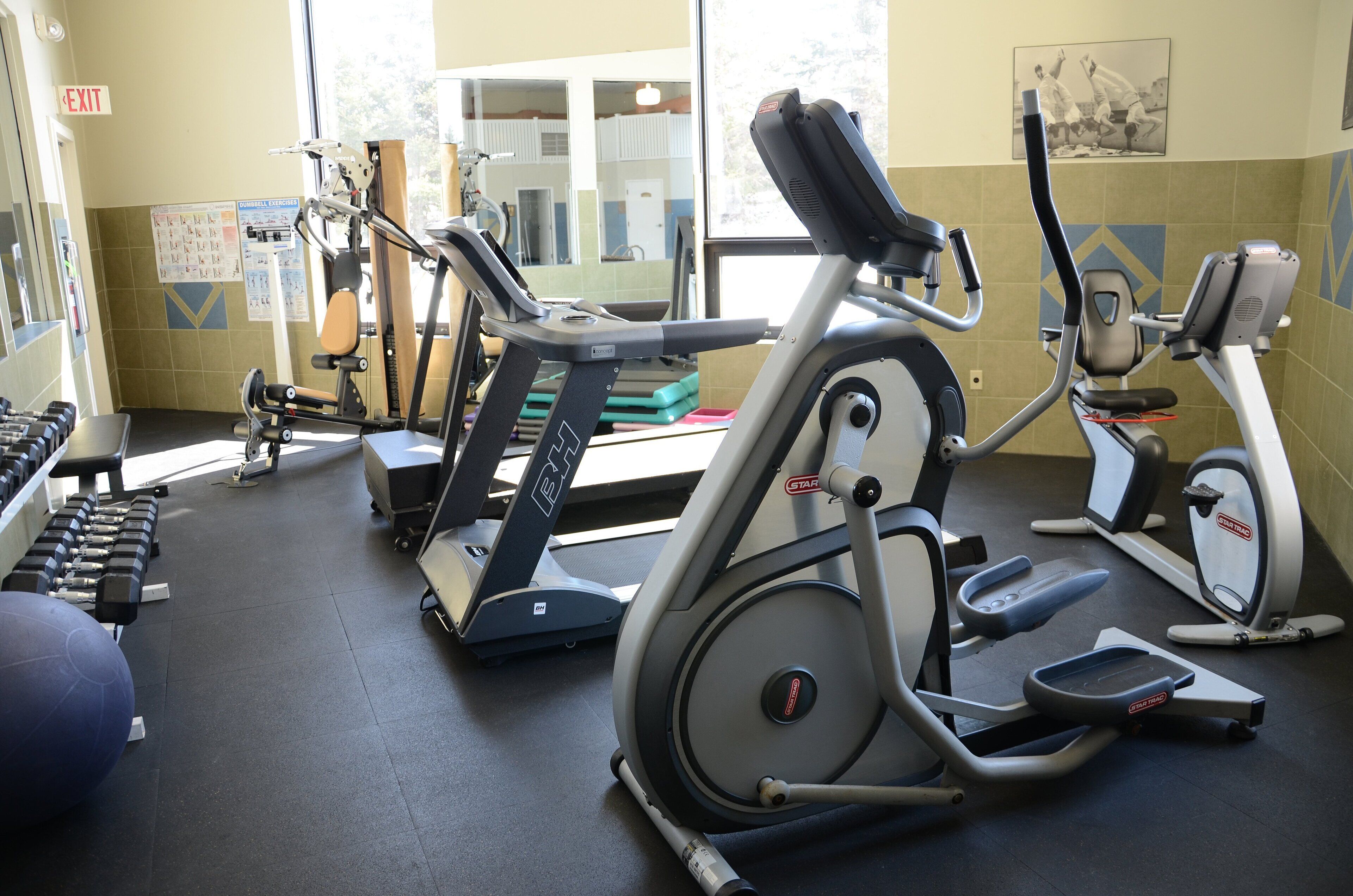 A gym with exercise equipment including treadmills, ellipticals, and dumbbells.