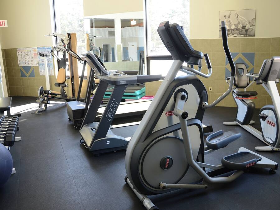 Ein Fitnessstudio mit verschiedenen Trainingsgeräten, darunter Laufbänder, ein Crosstrainer und Kurzhanteln.