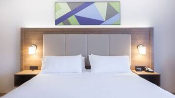 Habitación de hotel con una cama grande, dos mesitas de noche con lámparas, un cabecero moderno y una obra de arte geométrica en la pared.