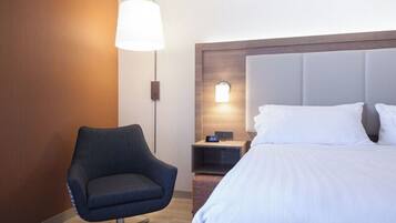 Une chambre d’hôtel avec un lit, une chaise, une table de chevet et une lampe fixée au mur.
