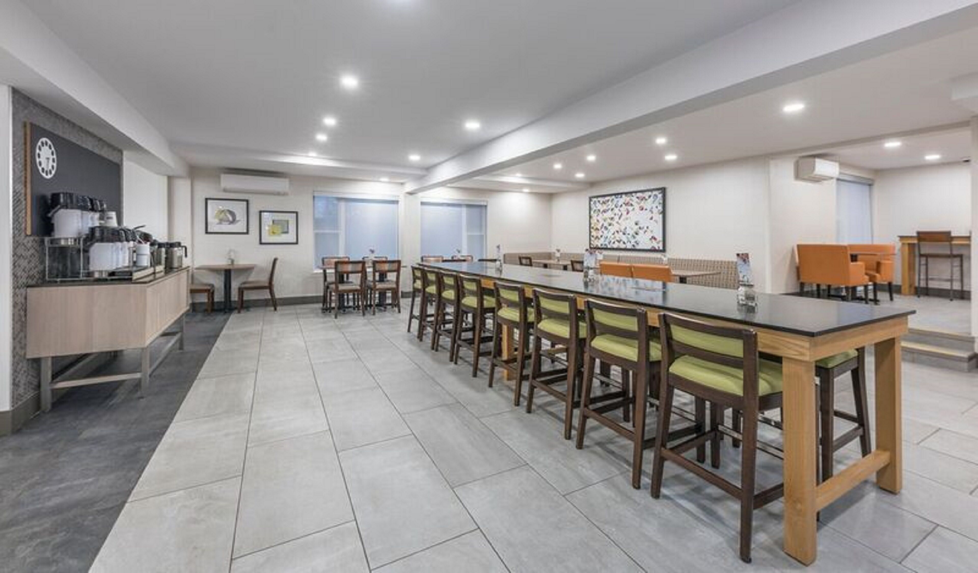 A modern dining area with a long table and chairs, a kitchen counter with appliances, and a large window.