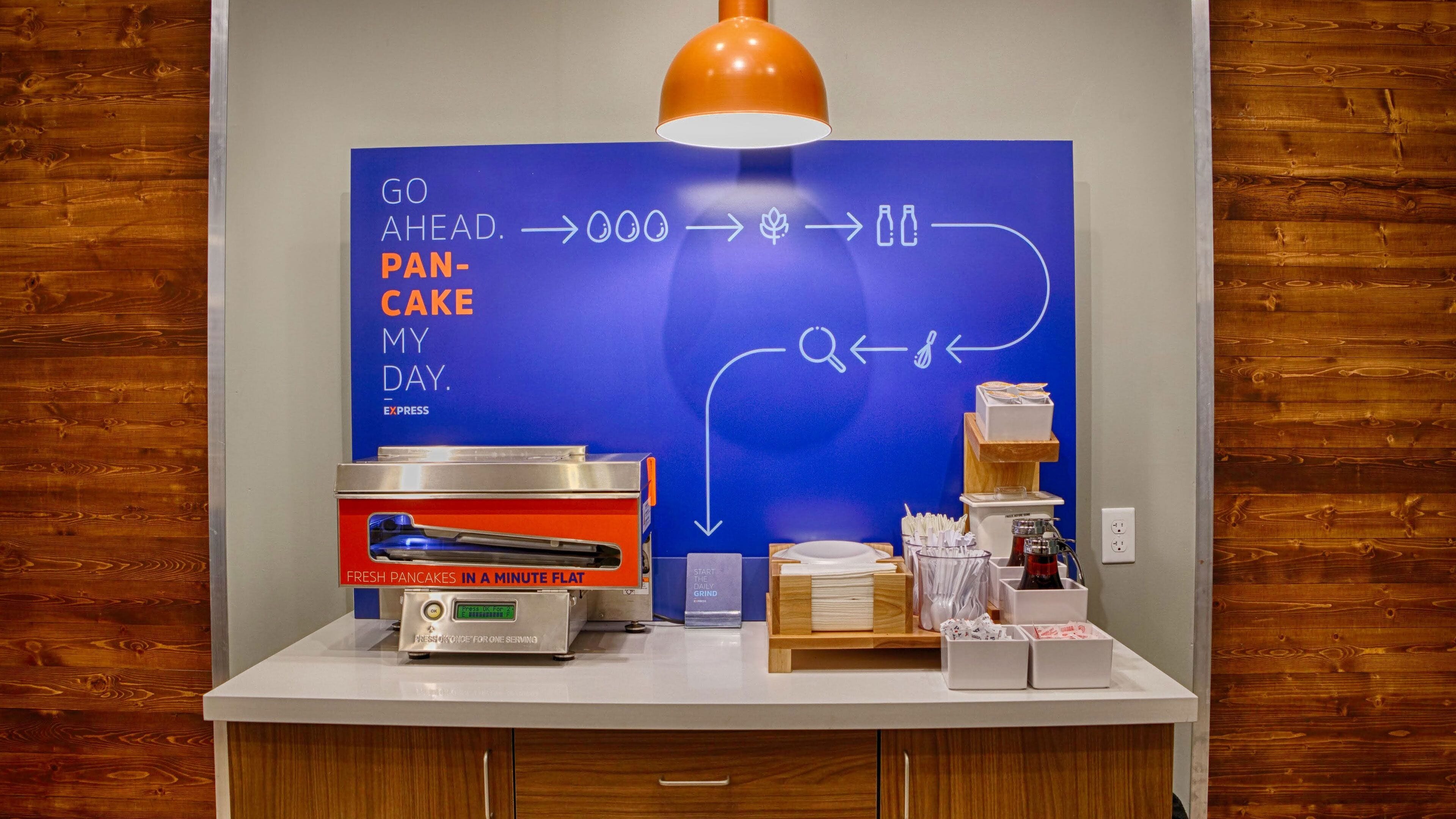 A breakfast station with a blue sign, a pancake maker, and a coffee machine.