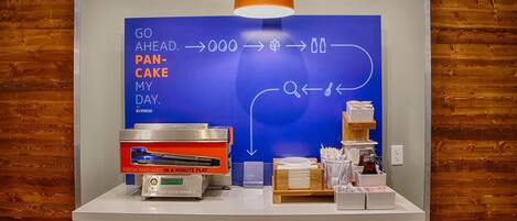 A breakfast station with a blue sign, a pancake maker, and a coffee machine.