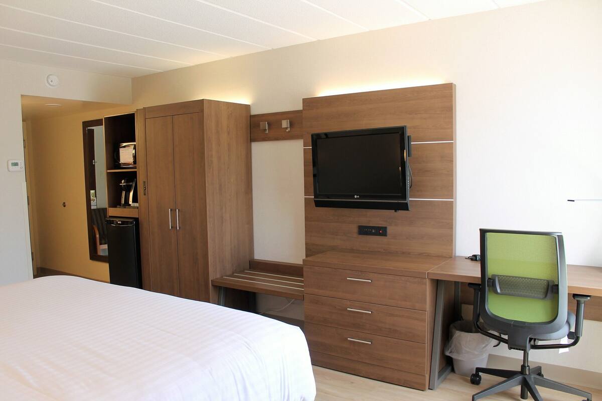 A hotel room with a bed, a desk with a computer and chair, a TV, and a wardrobe.