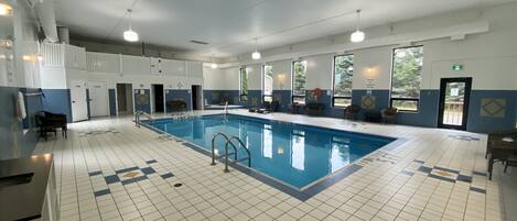 A large indoor swimming pool with clear lanes, a lifeguard chair, and a seating area with chairs.