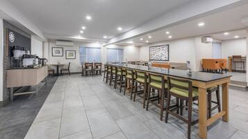 Un comedor moderno con una mesa larga y sillas, una encimera de cocina con electrodomésticos, y un reloj fijado en la pared.