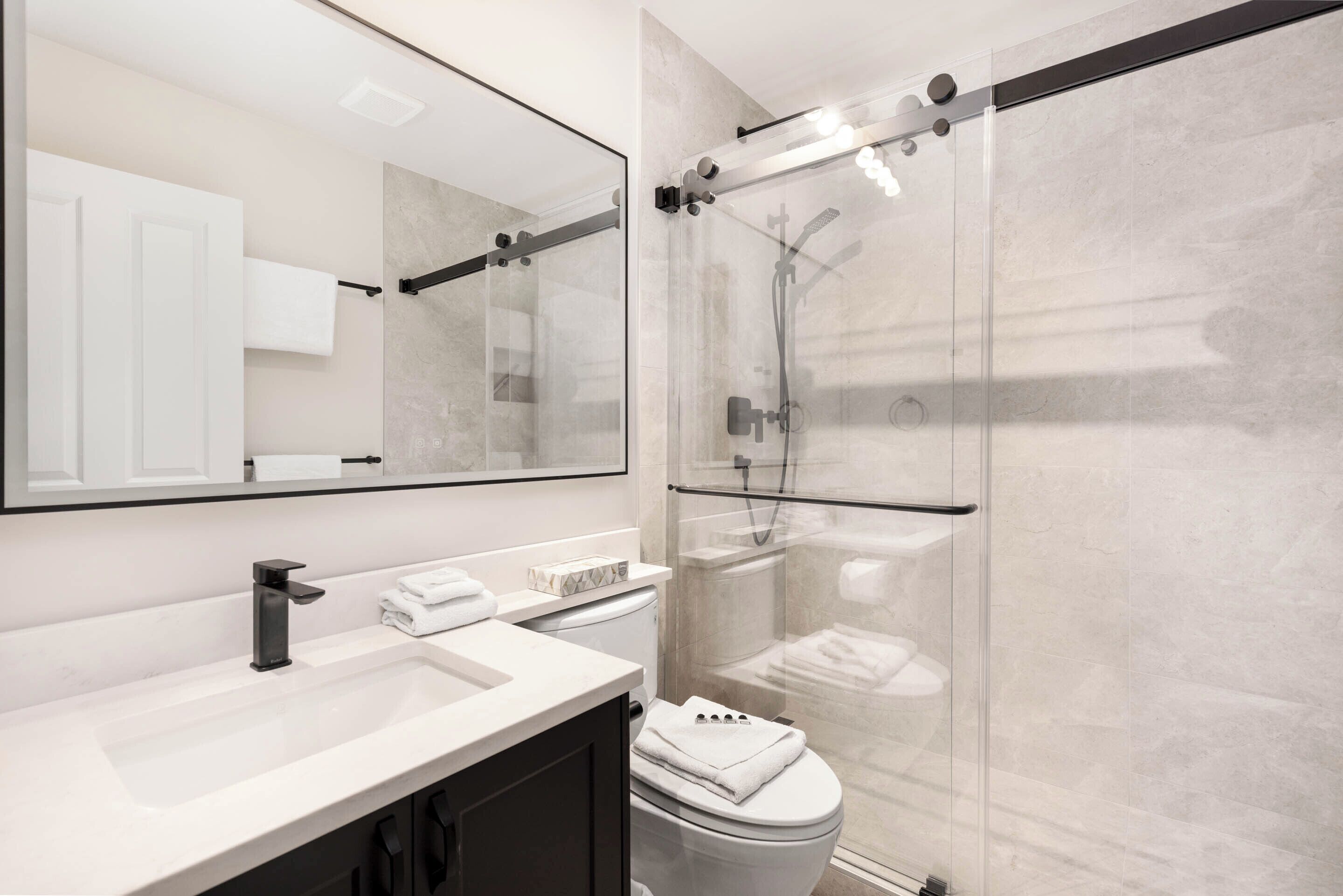 Un bany modern amb plat de dutxa envidriat, un lavabo blanc i un mirall gran.