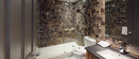A bathroom with a shower, toilet, and sink, featuring a tiled wall and a large mirror.