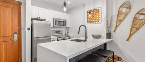 Una cocina moderna con armarios blancos, electrodomésticos de acero inoxidable, una isla grande con taburetes de bar y decoración en la pared.