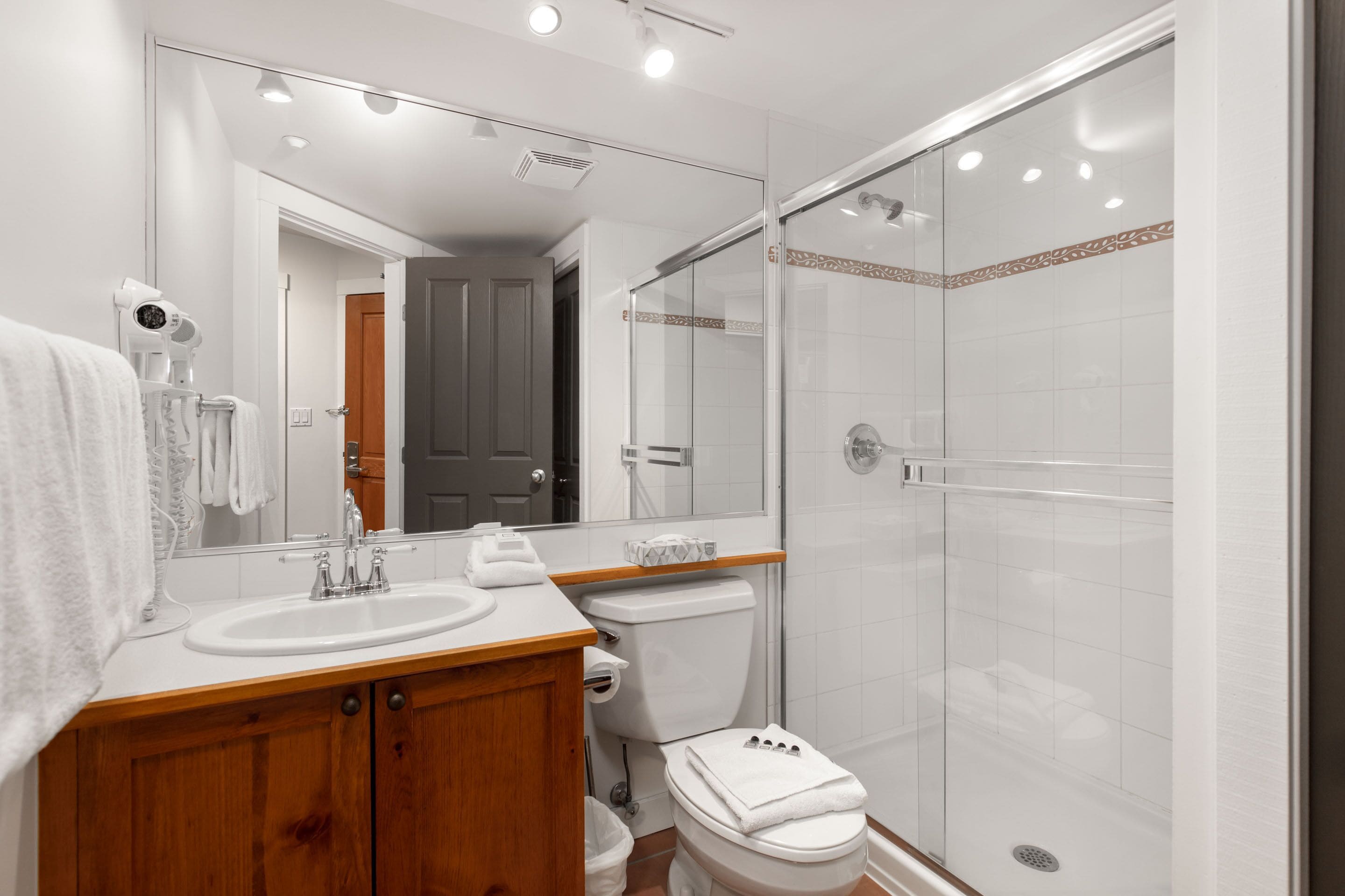 Une salle de bain moderne avec un meuble-lavabo en bois, un lavabo blanc et une douche à parois de verre.