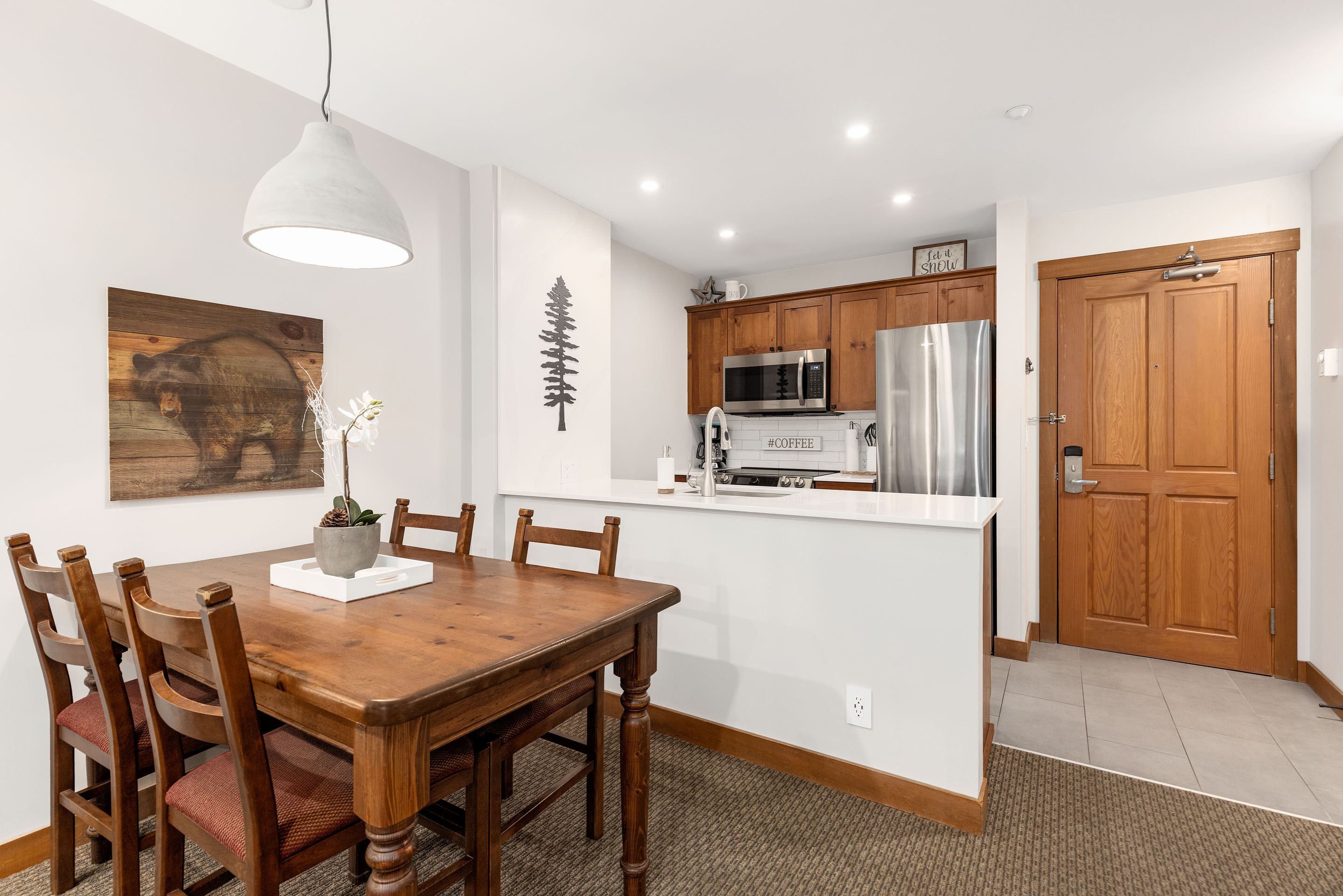 A dining area with a wooden table and chairs, a potted plant, and a wall-mounted light fixture.