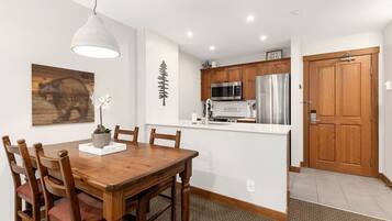 A dining area with a wooden table and chairs, a potted plant, and a wall-mounted light fixture.