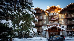 Una cabaña de varios pisos con fachada de piedra y balcones de madera, rodeada de árboles nevados.