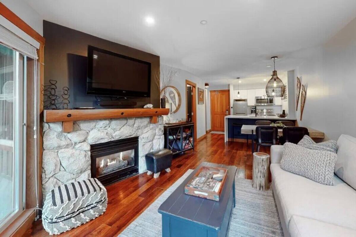 Una sala de estar moderna con chimenea de piedra, un televisor de pantalla plana montado encima y un rincón de estar acogedor con un sofá y un reposapiés.
