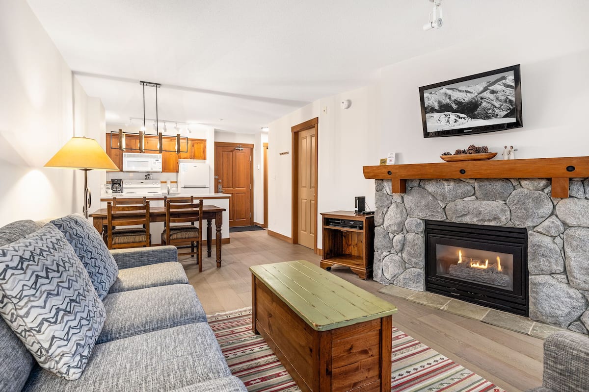 Una sala de estar con chimenea de piedra, un sofá, una mesa de centro y un comedor con mobiliario de madera.