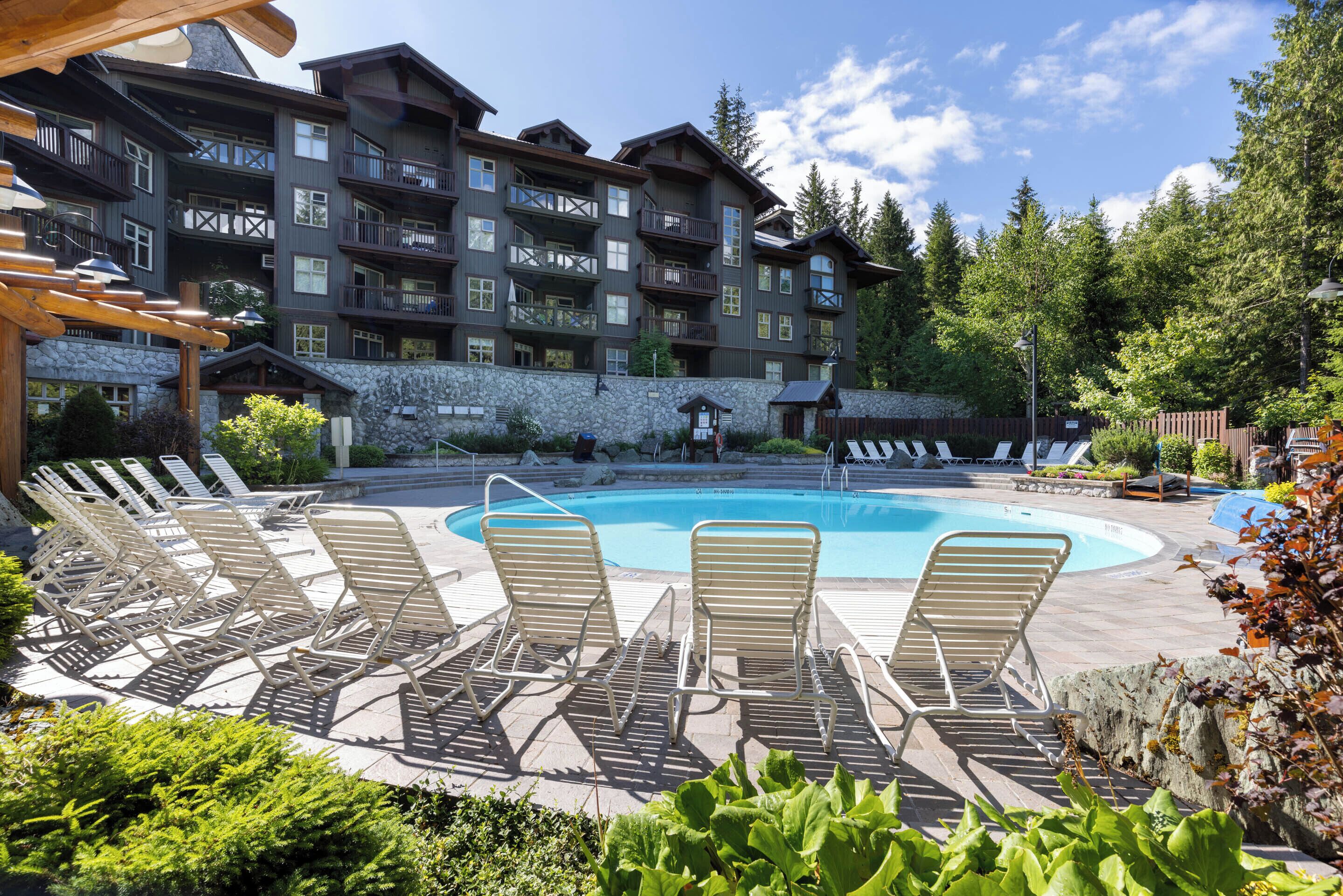 A hotel with a pool area, lounge chairs, and a stone facade.
