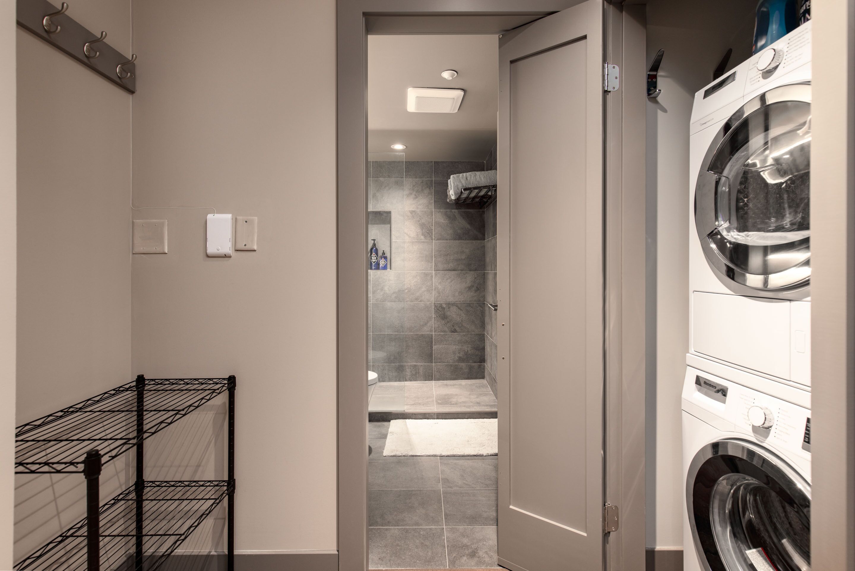 A laundry room with a washing machine and dryer, a metal shelf, and a tiled shower area.