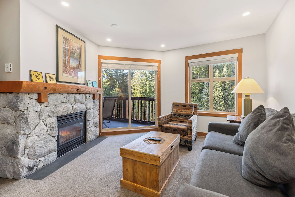 Una sala de estar acogedora con chimenea de piedra, un sofá, un sillón estampado y una mesa de centro.