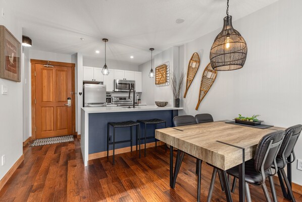 Una cocina moderna con una isla central, piso de madera y una zona de comedor con mesa de madera y sillas negras.