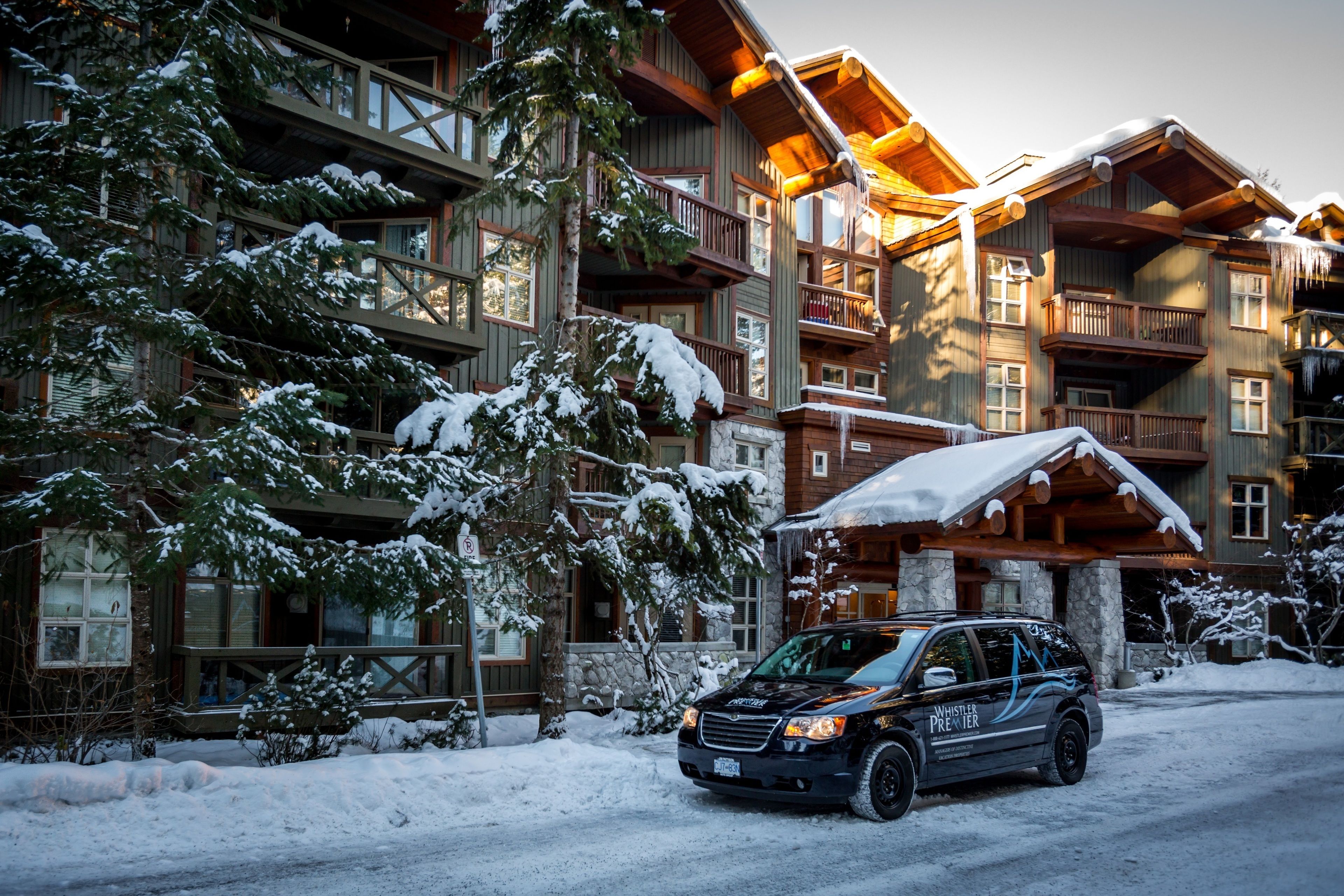 A multi-story lodge with a wooden exterior, balconies, and a snow-covered driveway.