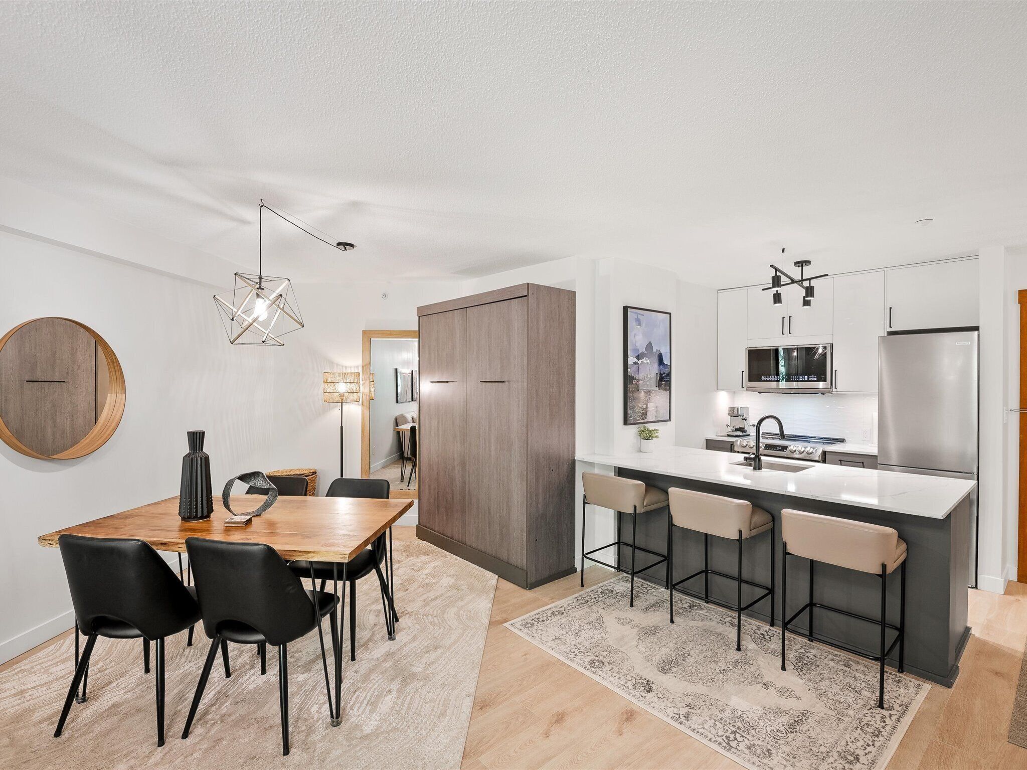 A modern kitchen with a central island, bar stools, and a dining area with a wooden table and chairs.
