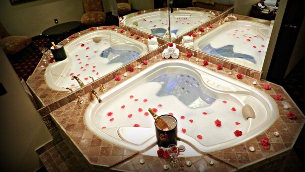 A luxurious bathroom with a large bathtub surrounded by rose petals and a champagne bottle.