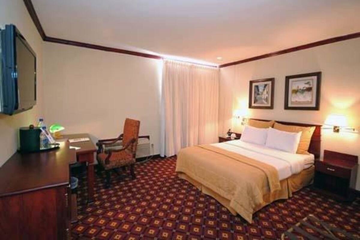 Een hotelkamer met een groot bed, een bureau met stoel, een bureaulamp en twee foto's in lijsten aan de muur.