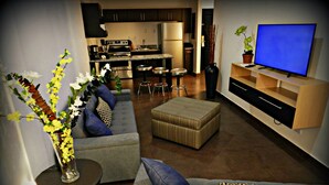 A modern living room with a grey sofa, ottoman, and a flat-screen TV on a wooden stand.