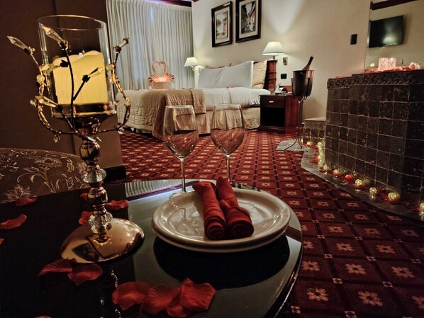 A hotel room with a bed, a bedside table with a lamp, a decorative glass, and a plate with rolled napkins.