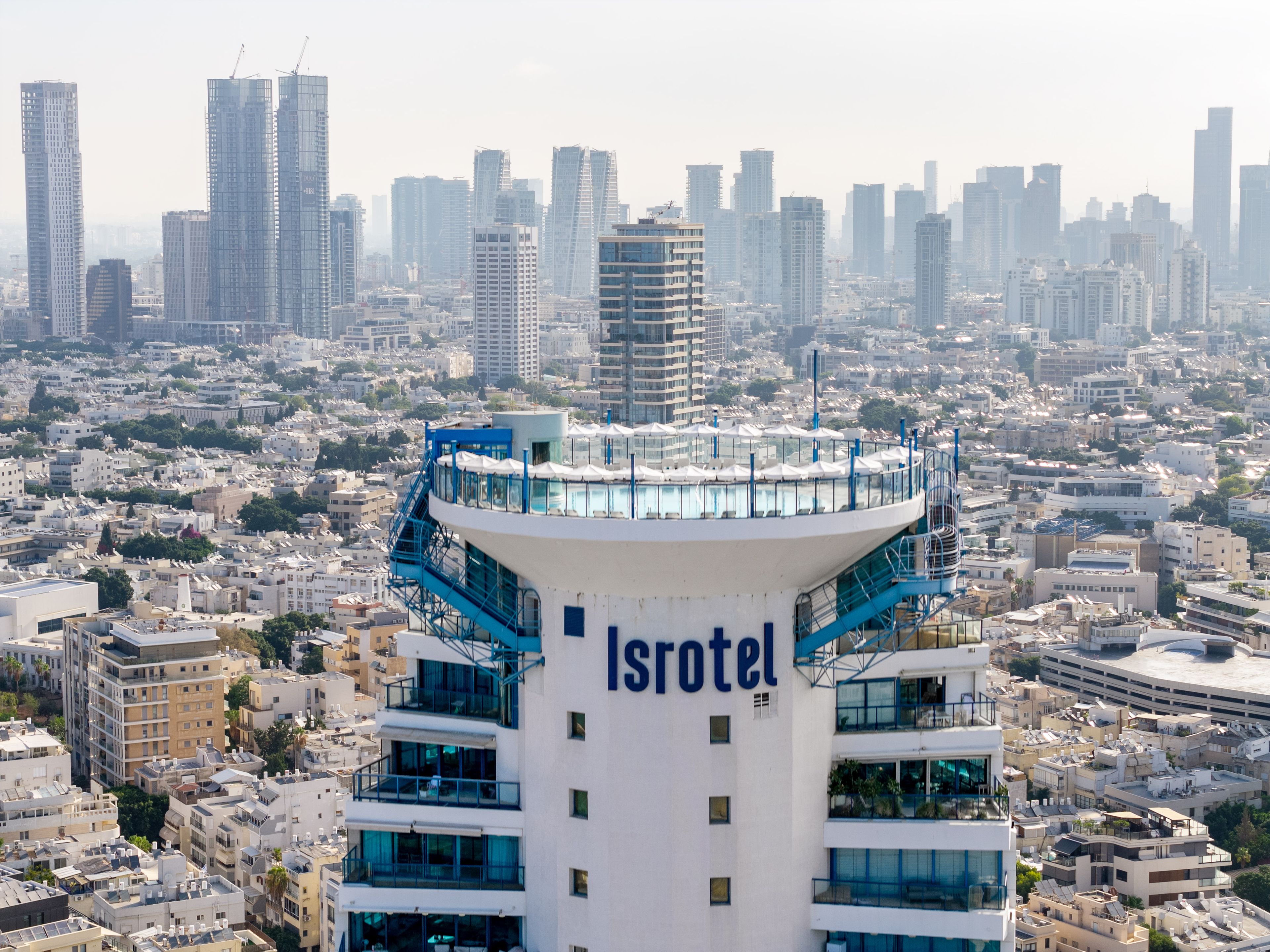 A high-rise hotel with a prominent 'Isrotel' sign, surrounded by a dense urban cityscape.