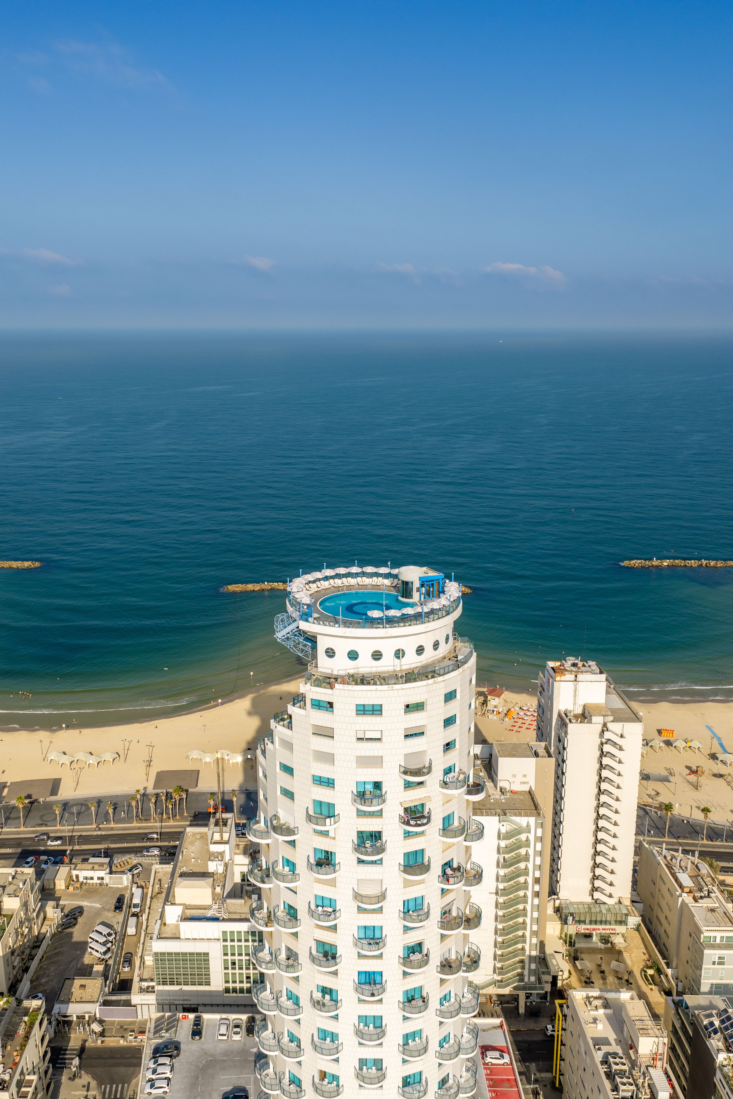 Un hotel de gran altura con una piscina circular en la azotea, una playa y una vista despejada del océano.