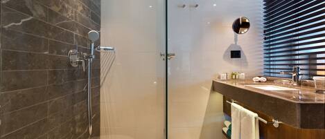 Un baño moderno con cabina de ducha de vidrio, zona de ducha con azulejos de mármol, tocador de madera con lavabo y espejo.