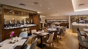 A modern restaurant with a central counter, multiple dining tables, and a kitchen area in the background. - Sea Tower by Isrotel Design (Tel Aviv)