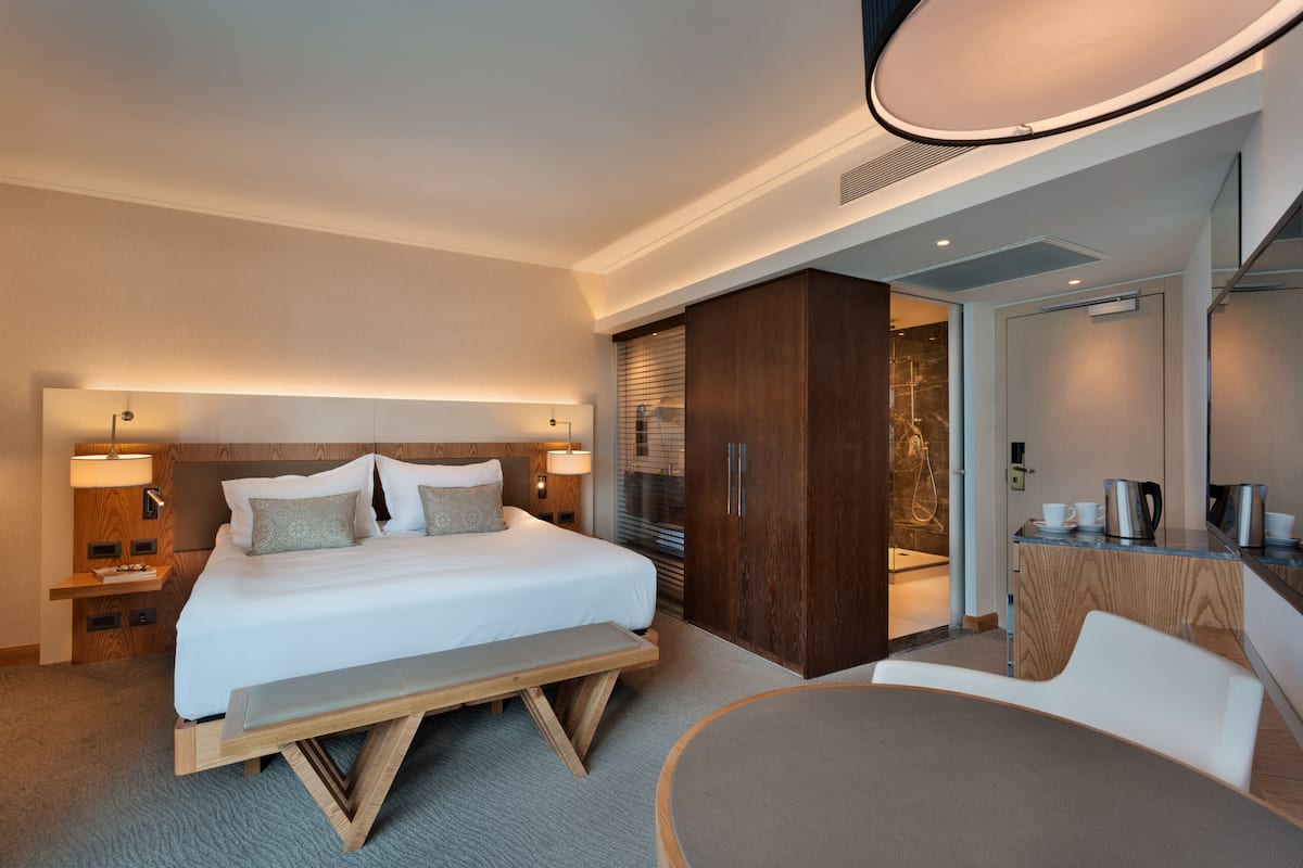 A modern hotel room with a large bed, bedside tables, a bench, a desk, and a chair.
