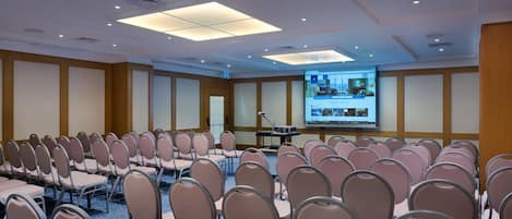 A conference room with rows of chairs, a projection screen, and a podium.