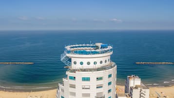 A multi-story hotel with a pool on the upper level, overlooking a beach and the sea.