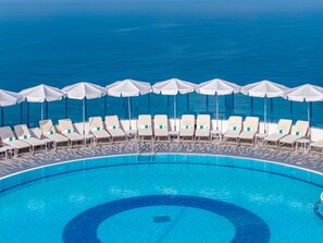 A poolside area with lounge chairs and umbrellas, overlooking a large body of water. - Sea Tower by Isrotel Design (Tel Aviv)