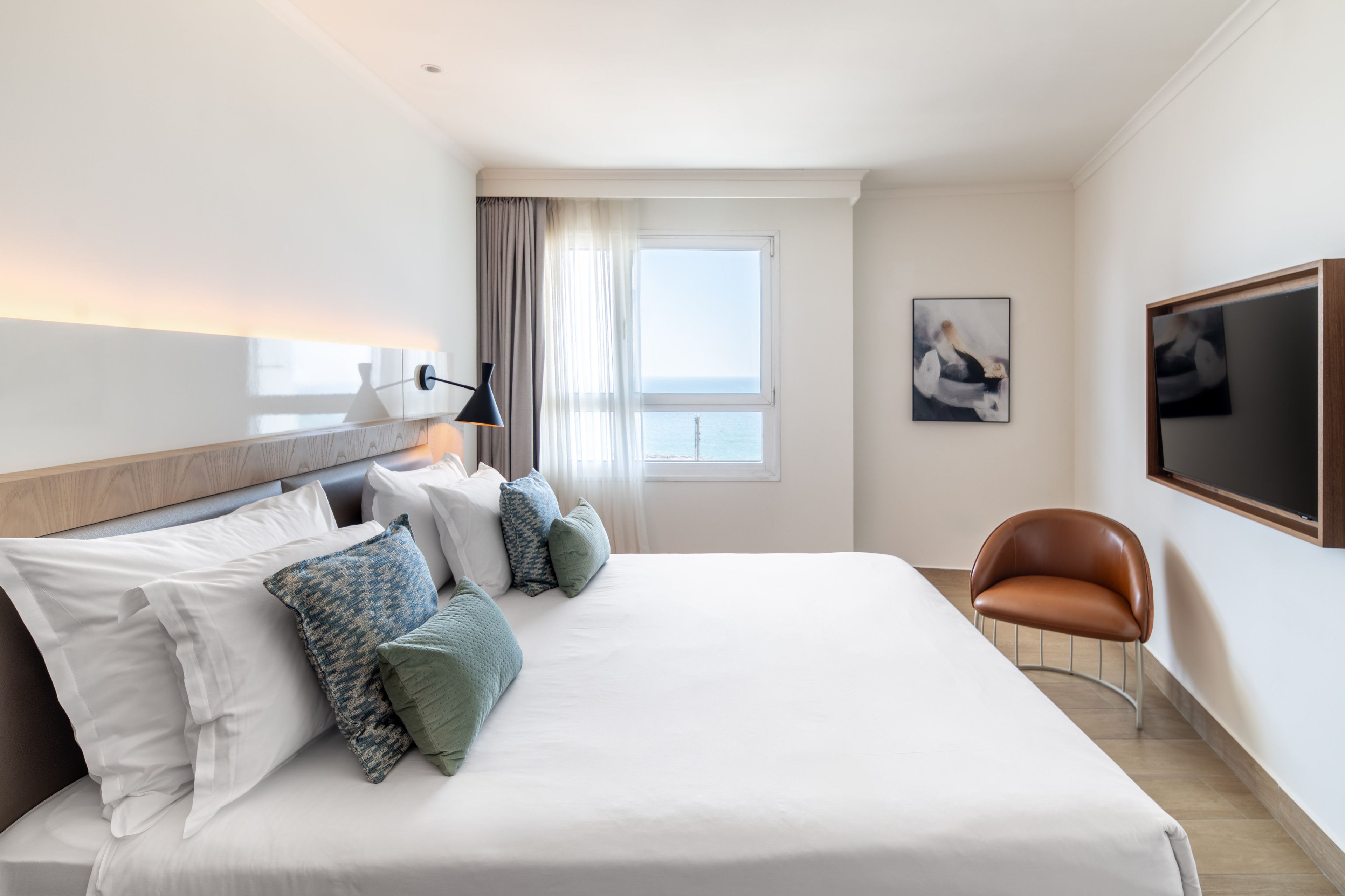 A hotel room with a large bed, a desk, a chair, a TV, and a window with curtains.