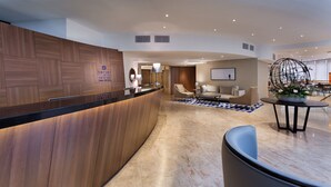A modern hotel lobby with a wooden reception desk, a seating area with sofas and a coffee table, and a decorative plant centerpiece. - Sea Tower by Isrotel Design (Tel Aviv)