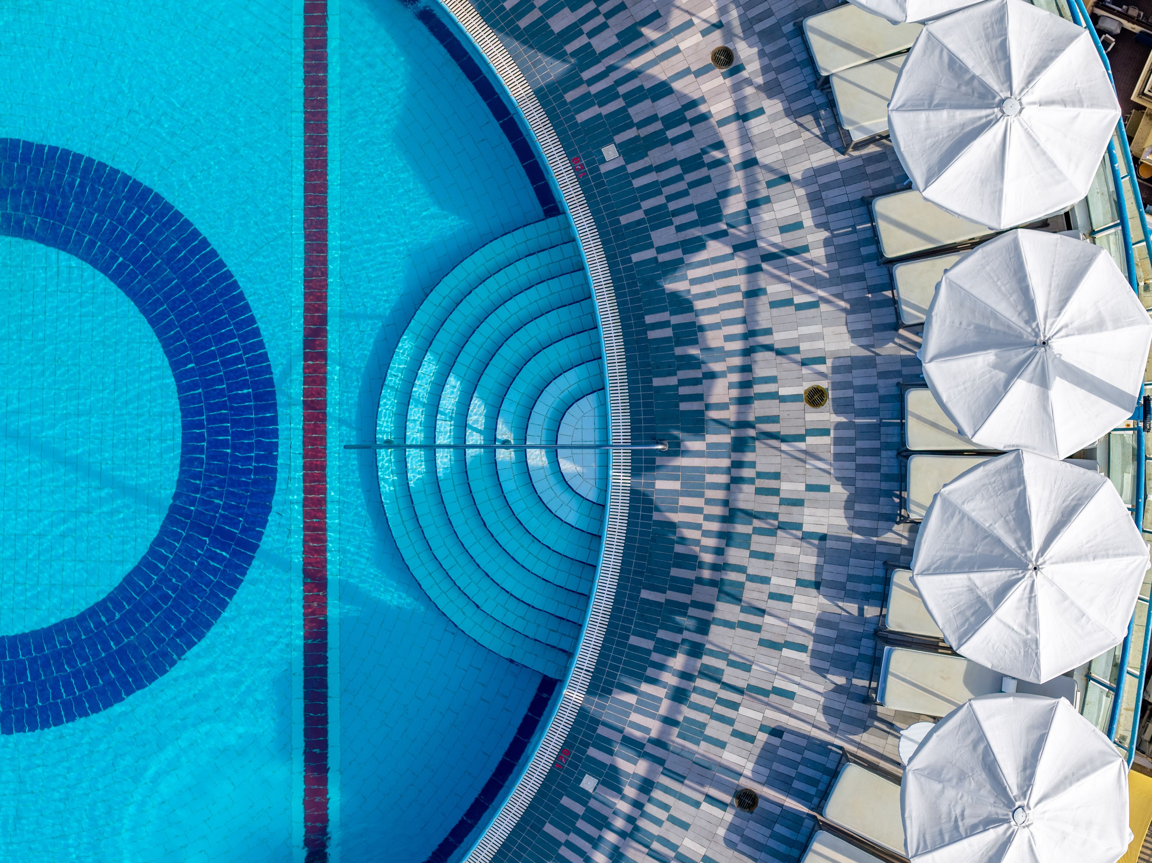 A swimming pool with a tiled edge and a tiled deck area with umbrellas.