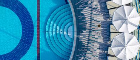 A swimming pool with a tiled edge and a tiled deck area with umbrellas.