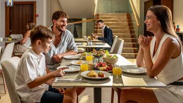 Eine Familie genießt das Frühstück an einem Tisch, im Hintergrund eine Treppe, modernes Interieur.