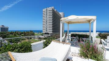 A rooftop terrace with a hammock, outdoor seating, and a view of the ocean and cityscape.