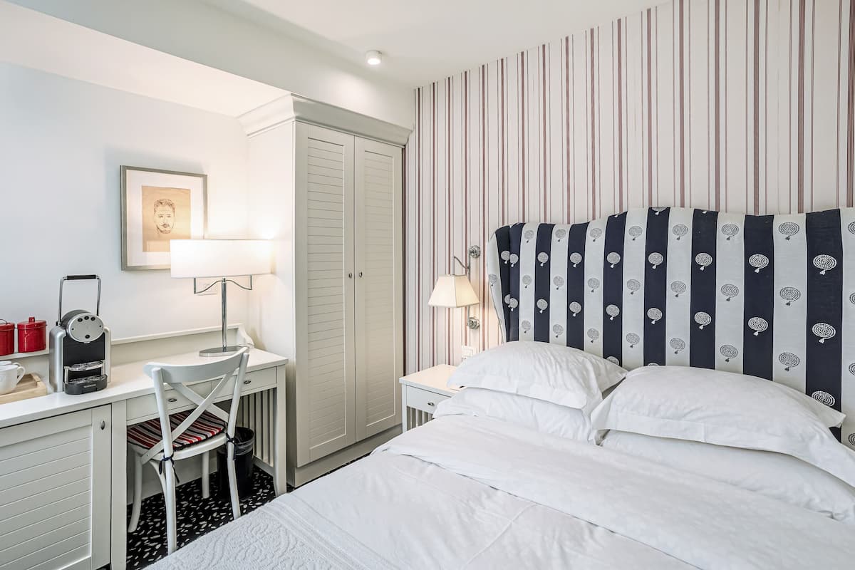 A hotel room with a bed, a desk with a chair, a lamp, and a wardrobe.