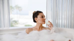 A person in a bathtub filled with bubbles, with a window in the background. - Shalom Hotel & Relax - an Atlas Boutique Hotel (Tel Aviv)