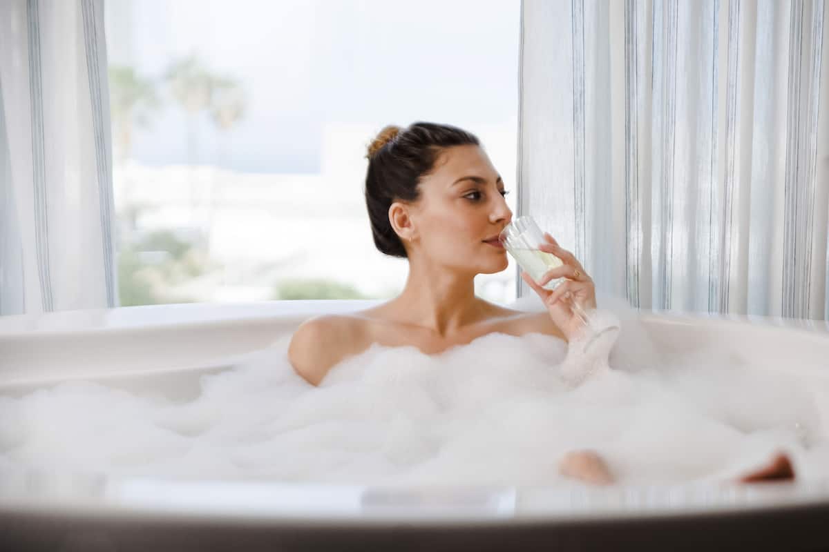 A person in a bathtub filled with bubbles, with a window in the background.
