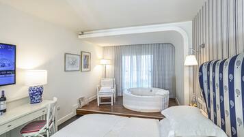 Una habitación de hotel con una cama, un escritorio con silla, una mesita con lámpara, un ventanal con cortinas y una bañera de hidromasaje.