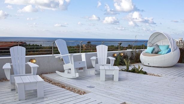 A rooftop deck with white Adirondack chairs, a white wicker sofa, and a view of the ocean. - Shalom Hotel & Relax - an Atlas Boutique Hotel (Tel Aviv)